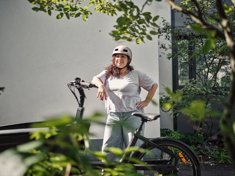 Eine Frau lehnt stolz an ihrem Lastenrad und trägt einen Helm.